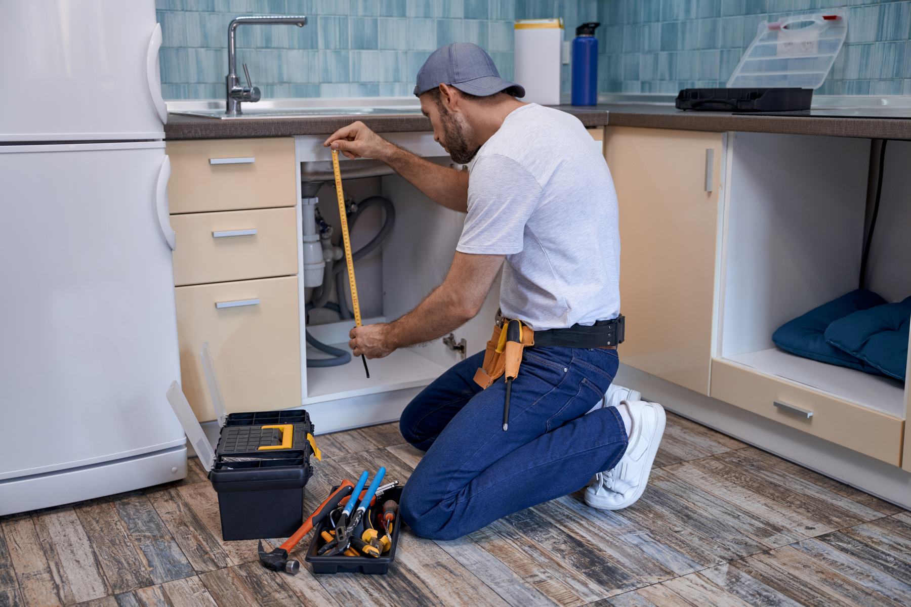 A plumber working on the pipework beneath a kitchen sink.