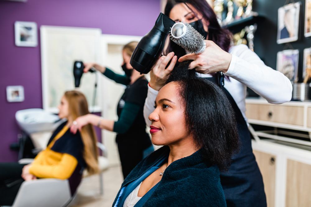 A stylist blow-drying a client's hair in a salon.